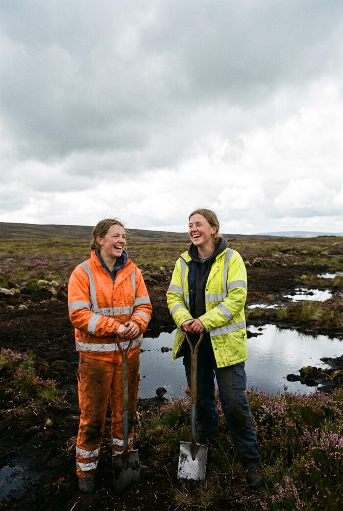 Two young women in hi-vis on a windswept moorland peat restoration site